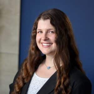 A corporate headshot of Kayla Hampe standing in front of a navy blue wall