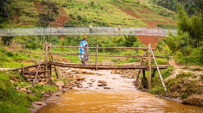 A woman on a temporary bridge in Rwanda while a permanent pedestrian bridge is being built behind her