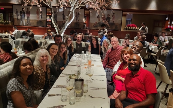 A group photo at a long dining table inside a steakhouse to celebrate Doug Norman's retirement sendoff and the new leadership for our Florida office