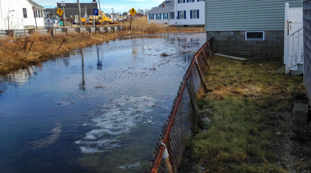 Image in Hampton, New Hampshire of high waters directly up against homes. A chain link fence is also in the foreground.