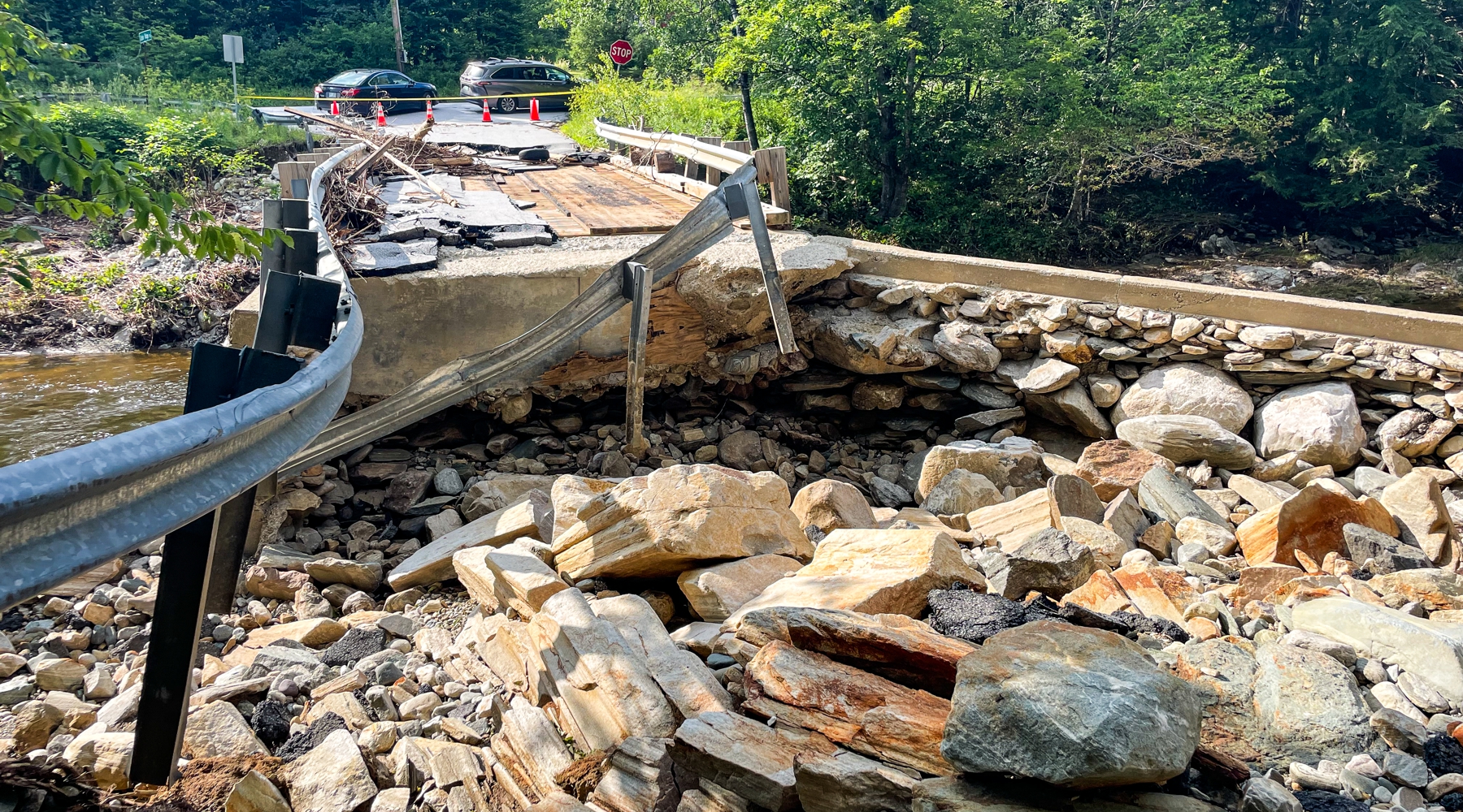 A project photo taken after some of Vermont's July Storms in 2023. The photo features a collapsed bridge amongst piles of rocks and a broken guardrail.