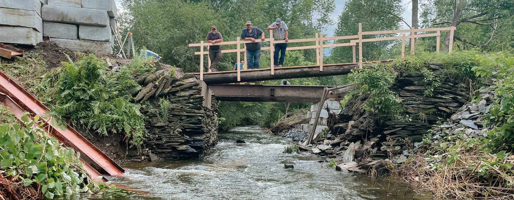 As part of Vermont's July storms, three people stand on a temporary bridge to assess damage in Londonderry Vermont. The photographer is downstream looking up at the people on the bridge.