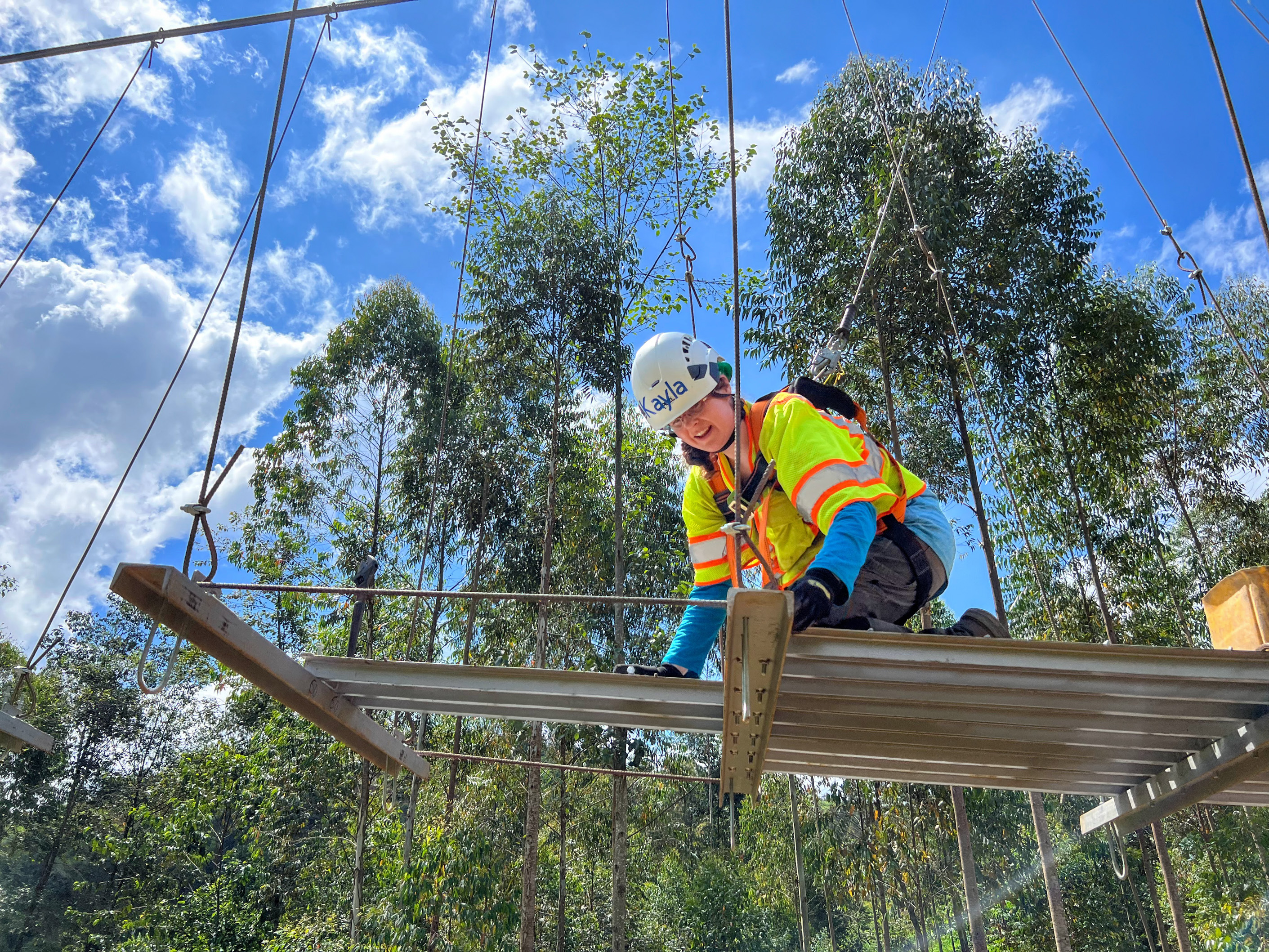 Kayla Hampe in a yellow vest and hard hat building out a bridge in Rwanda - the sky and clouds behind her.
