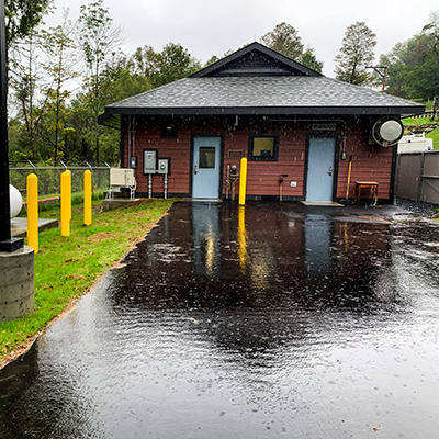 A photo of a newly-constructed building (small) on a rainy day with shiny, black pavement in the forefront.