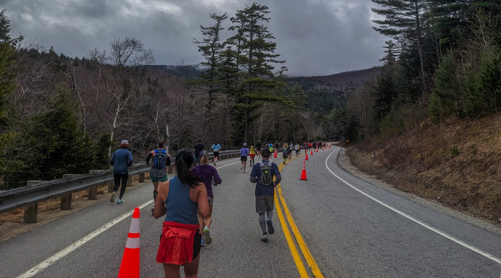 This photo was taken during the race. It shows Nick's perspective and can see the racers in front of him on the road. There are traffic cones and the yellow road stripes visible. The sky is cloudy.