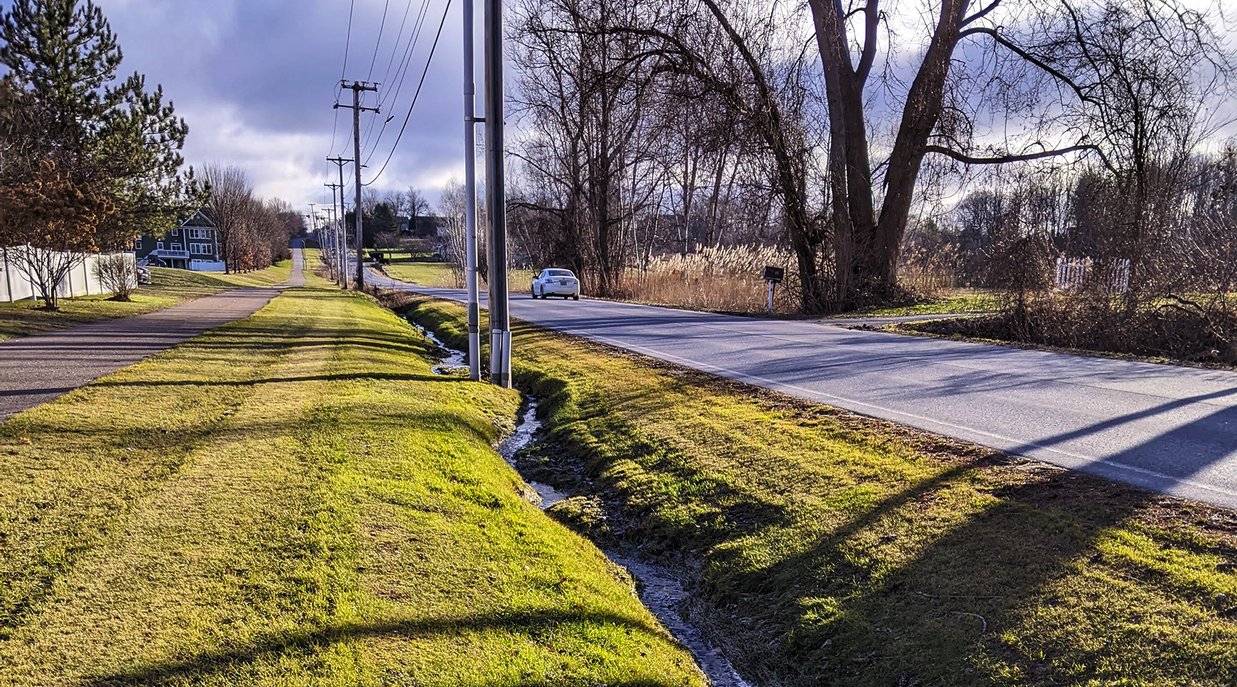 A sunny picture of a road and a few telephone poles in South Burlington, Vermont. Shadows lay across the ground from the trees.