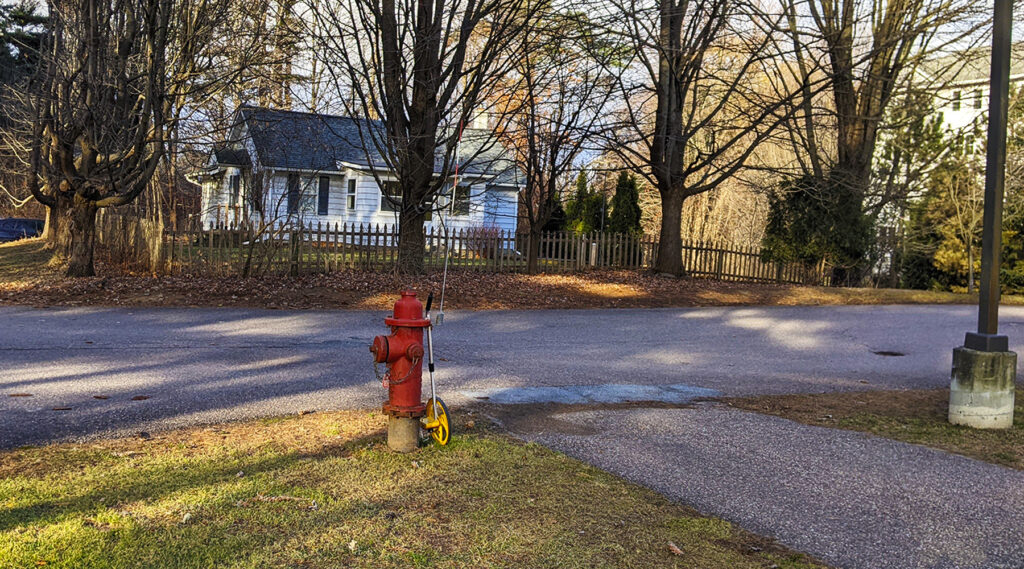 An image of a fire hydrant and an engineering tool along a road. The sun is coming in and casting shadows of trees on the ground. It's fall.