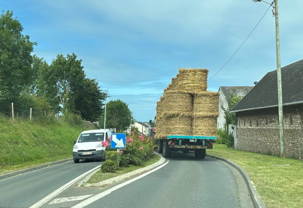 Truck piled with hay easily negotiates around a lateral shift planted with flowers at a gateway near Étretat, France