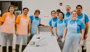 A photo of our team volunteering at NH Food Bank. Our team is in their volunteer shirts, wearing hair masks and aprons.