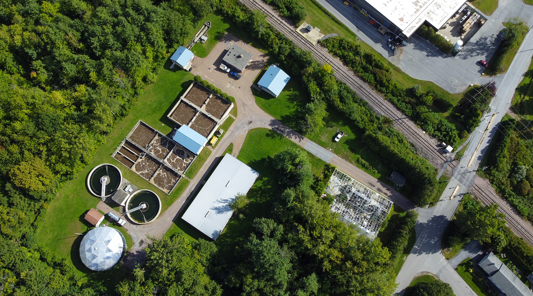 Aerial image of the entire Bartlett Bay WWTF. The sun is shining and there is lush greenery all around the plant.