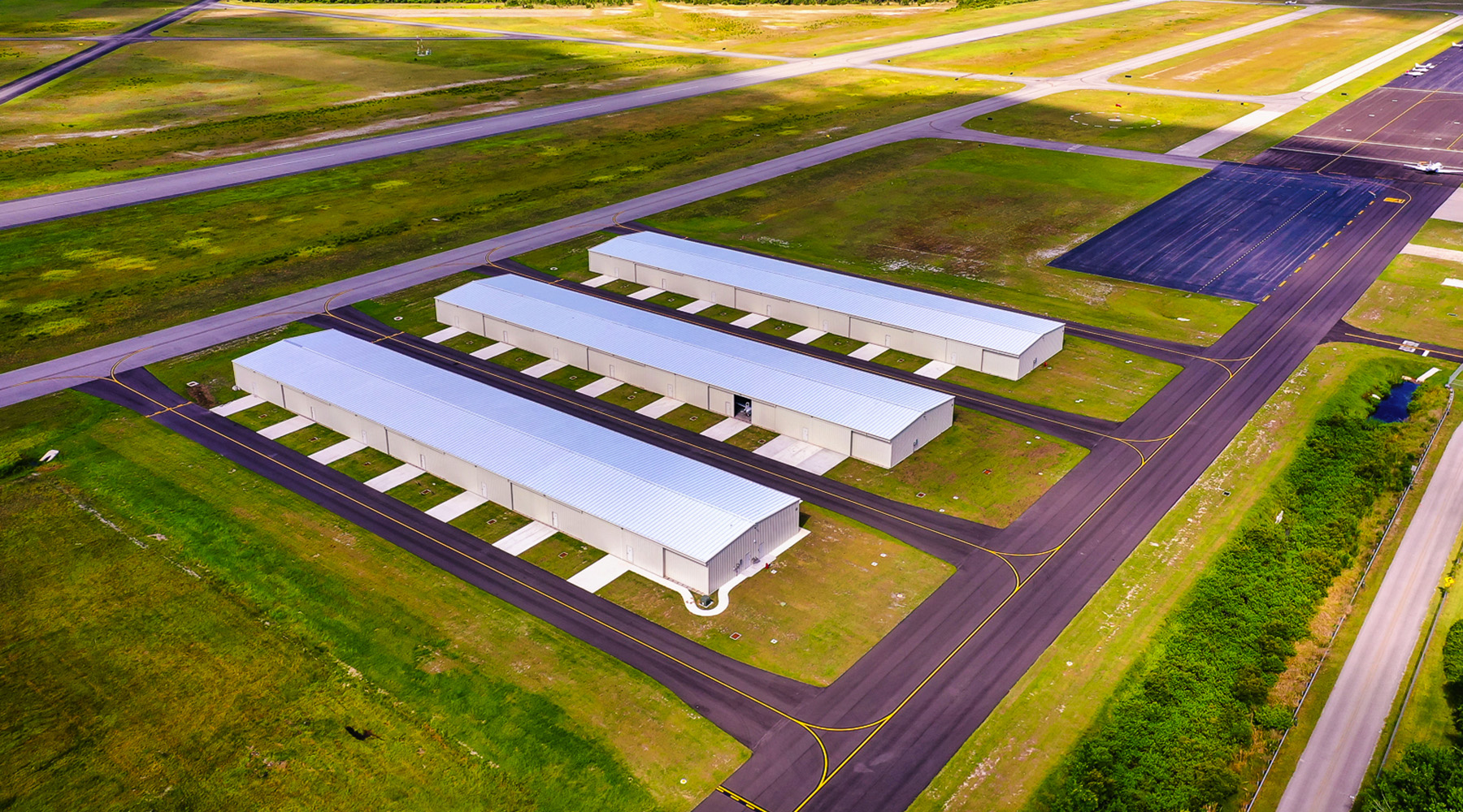 An aerial image of the T-Hangars at Flagler Executive Airport. The sun is shining and the grass is a vivid green landscape around the project bounds.