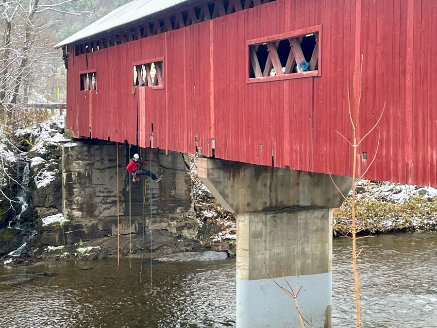 A Hoyle Tanner Engineer Performing Rope Access Inspection on a Covered Bridge in New England.