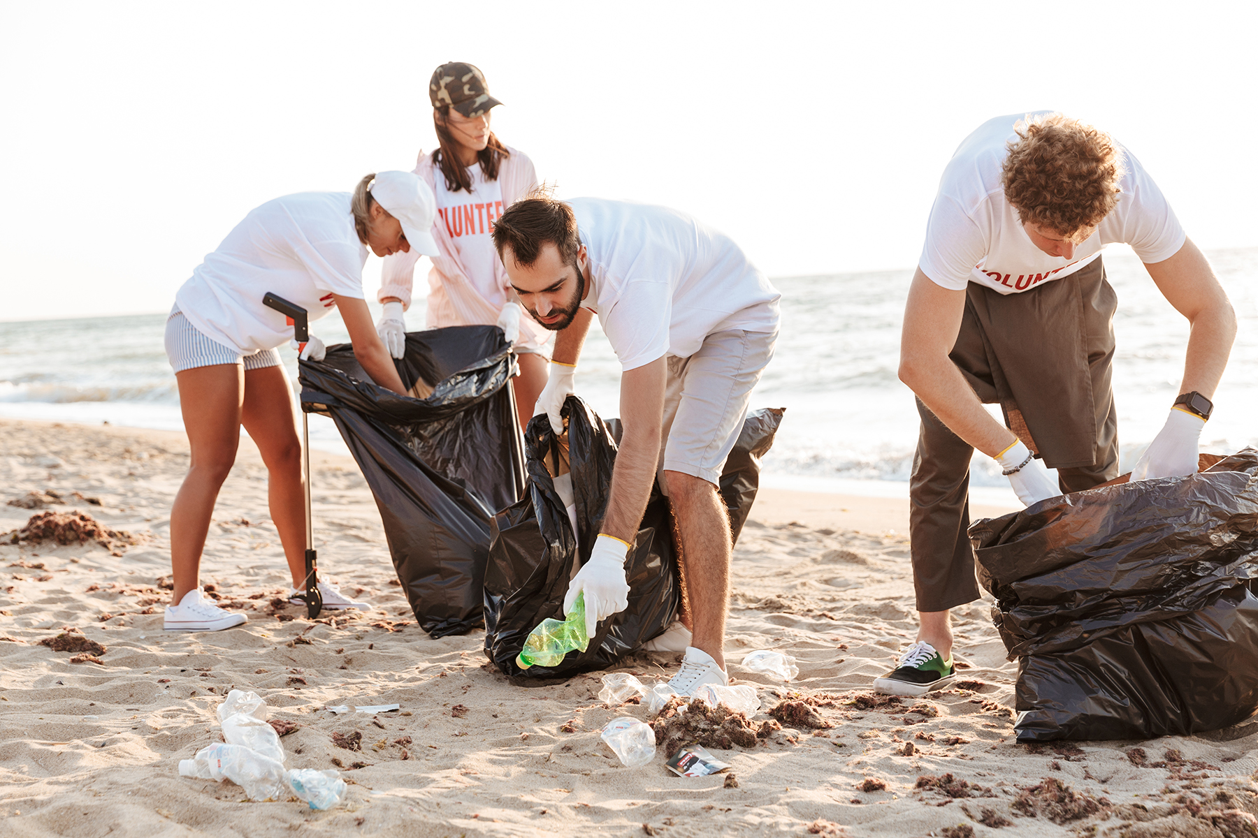 Photo of  volunteers people cleaning beach from plastic with trash bags at seaside