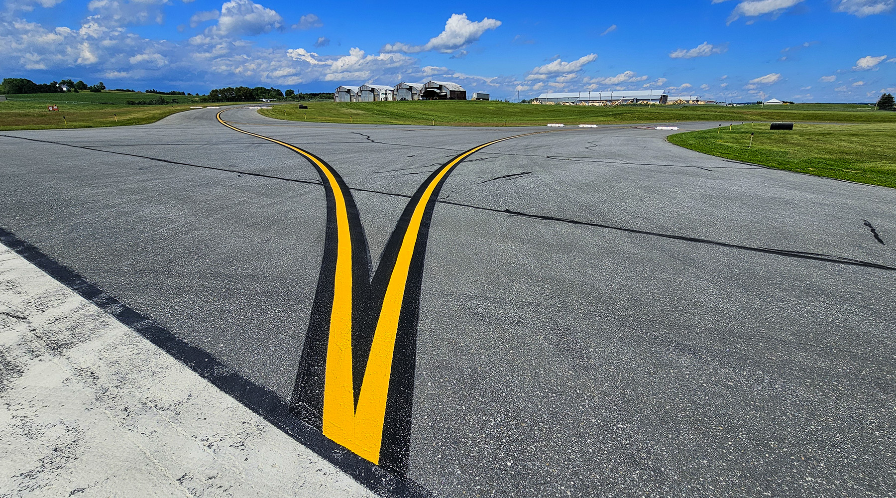 Photo of yellow striping splitting in two different directions on pavement at an airport.