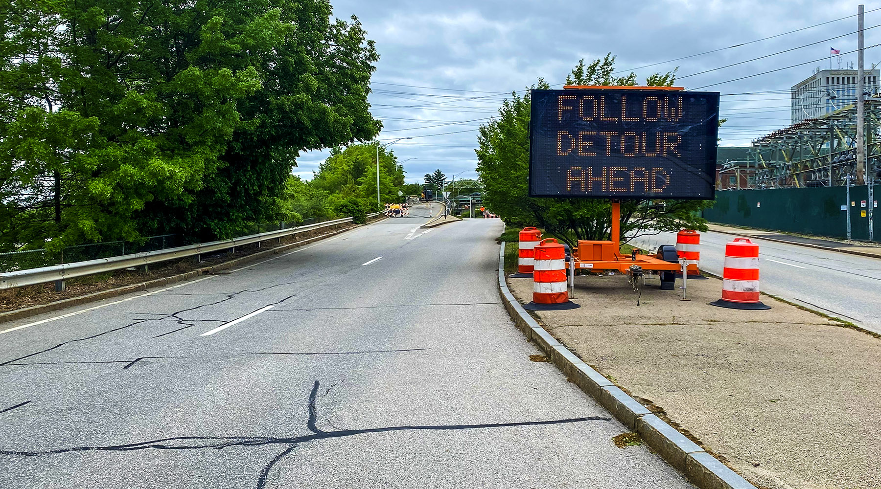 A photo from the Amoskeag Bridge construction with a Work Zone sign to the right (sitting atop a median) that says "Follow Detour"