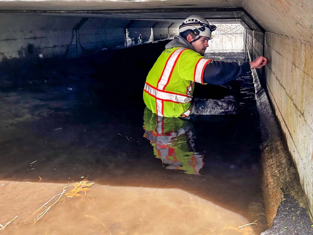 One of our engineers inspecting a bridge in Massachusetts. He's in a safety vest underneath a bridge with water past his waist.