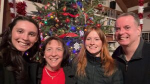 Bill is to the far right smiling at the camera standing next to members of his family. The background is decorated for Christmas.