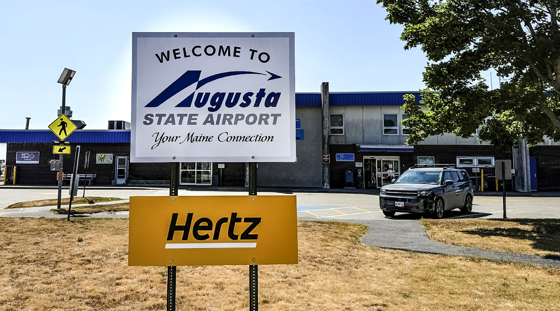 A sign that says Augusta State Airport in front of the airport. It's a sunny day with blue skies.