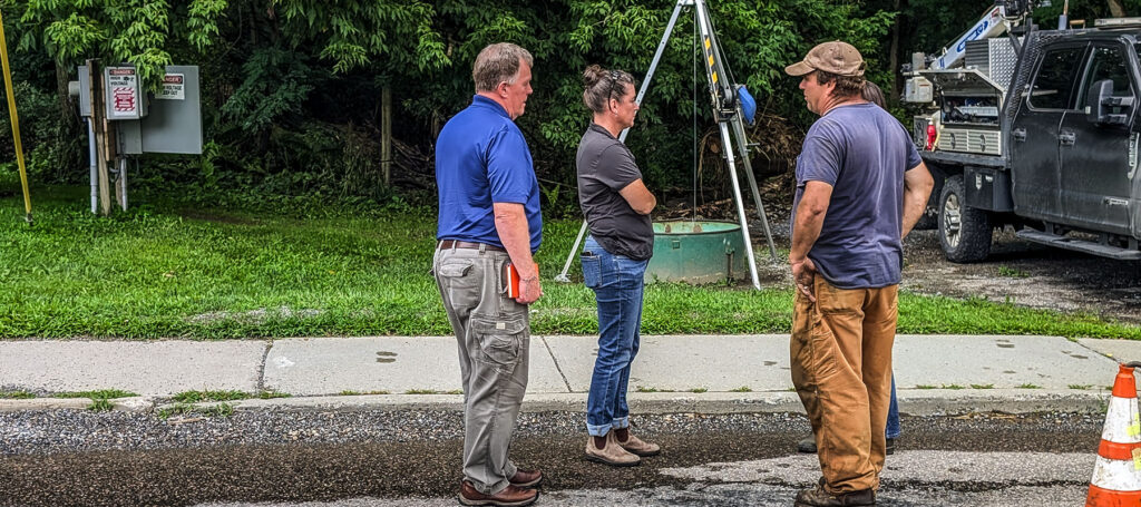 The Hoyle Tanner team is discussion the pump station project, standing near an open man hole and looking at infrastructure.