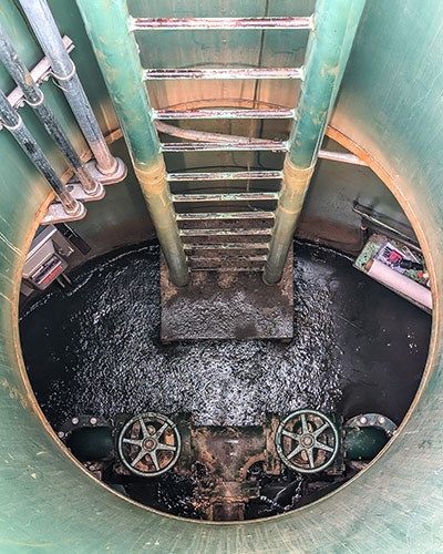 Looking down into wastewater infrastructure. There's a green ladder that changes color and water at the bottom.
