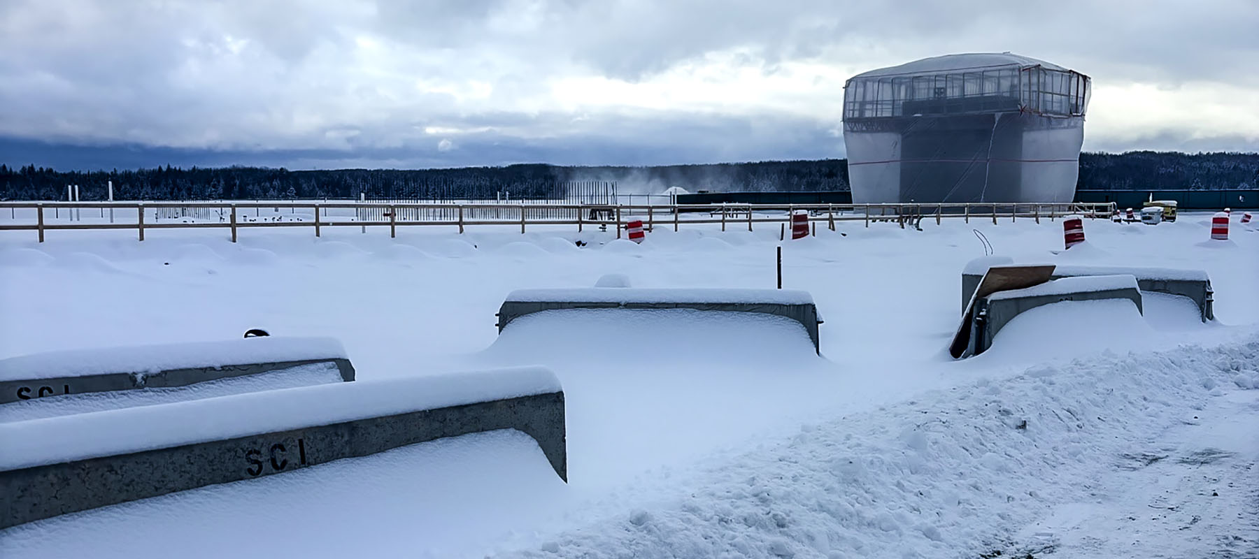 An image of construction materials stacked up during winter at an airport after winter shutdown. There is snow all over the ground and the photo is cool-leaning in tone.