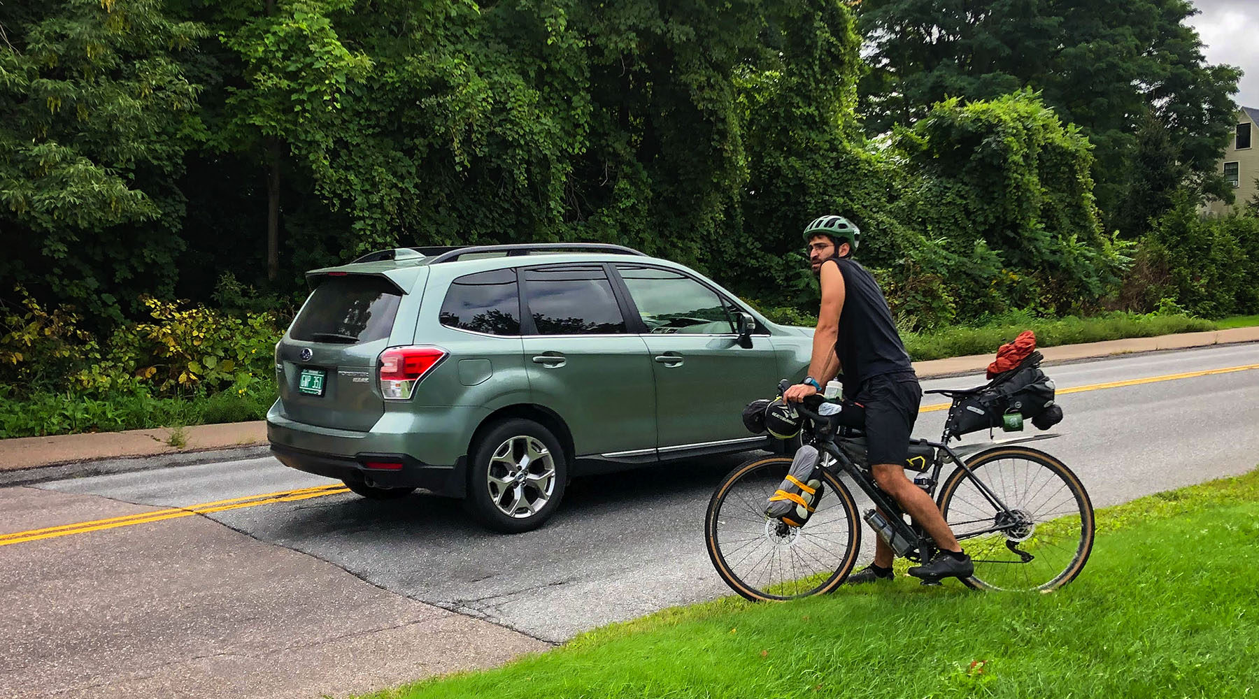A cyclist is pictured on their bike attempting to cross a road while a car passes by.
