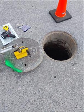 Sewer manhole with cover off next to traffic cone and tools